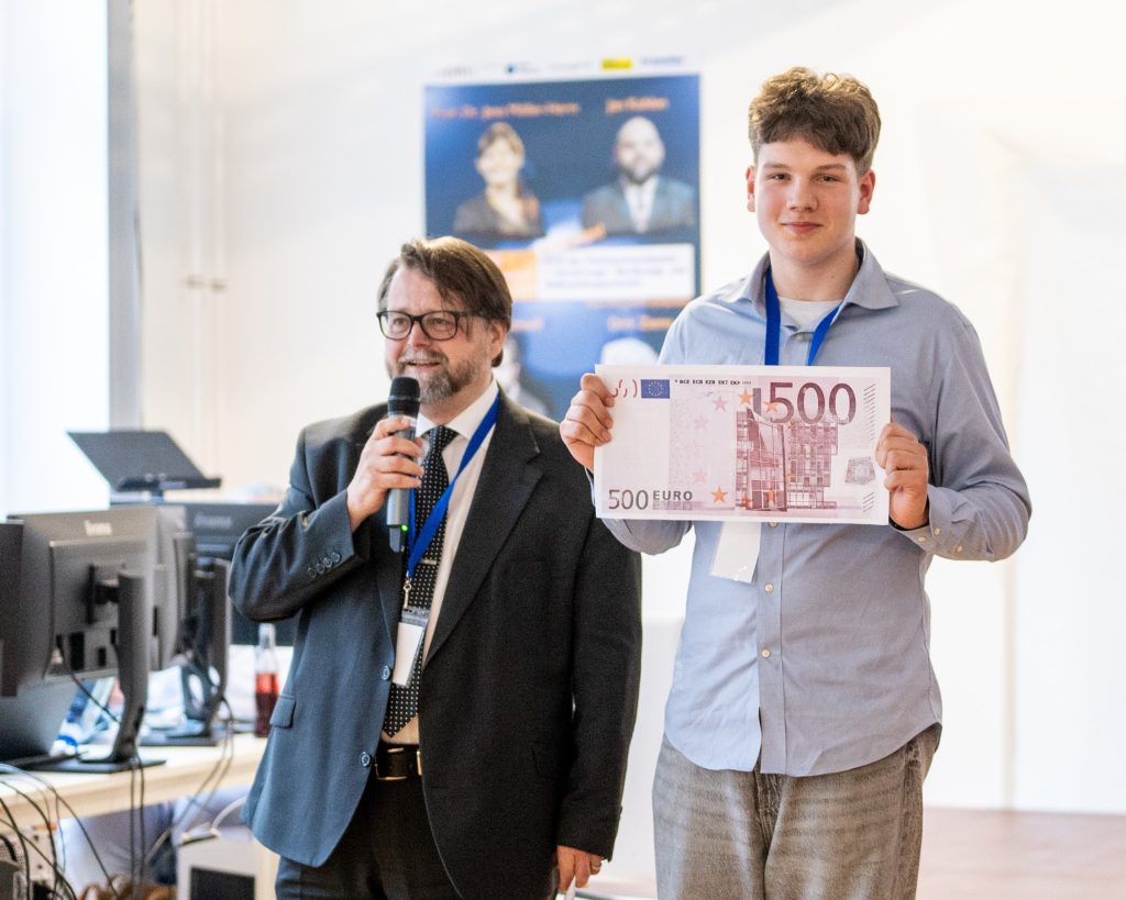 A moderator with microphone and a happy, smiling young man holding a 500 € banknote he won for pitching his business model at eye square's pitch night in July. 2024.